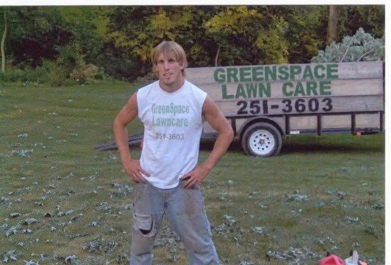 Early GreenSpace LawnCare photograph with a worker wearing GreenSpace apparel standing beside a branded trailer
